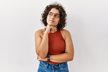 Canvas Print - Young hispanic woman wearing glasses standing over isolated background with hand on chin thinking about question, pensive expression. smiling with thoughtful face. doubt concept.