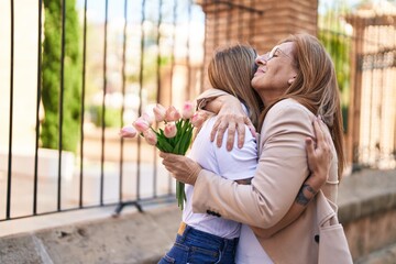 Poster - Mother and daughter hugging each other holding bouquet of flowers at street