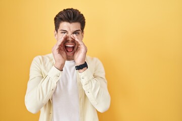 Sticker - Young hispanic man standing over yellow background shouting angry out loud with hands over mouth