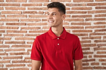 Canvas Print - Young hispanic man standing over bricks wall smiling looking to the side and staring away thinking.