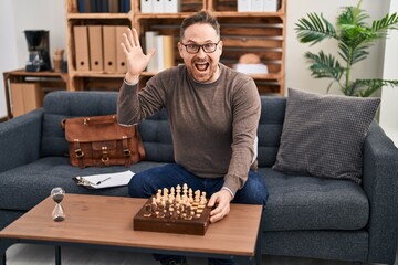 Poster - Middle age caucasian man playing chess sitting on the sofa celebrating victory with happy smile and winner expression with raised hands