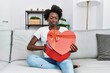 African young woman opening romantic gift relaxed with serious expression on face. simple and natural looking at the camera.