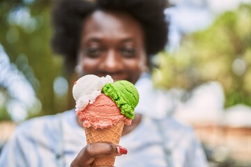 Wall Mural - Young african woman smiling eating ice cream at park