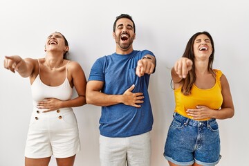 Wall Mural - Group of young hispanic people standing over isolated background laughing at you, pointing finger to the camera with hand over body, shame expression