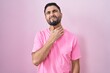 Hispanic young man standing over pink background touching painful neck, sore throat for flu, clod and infection