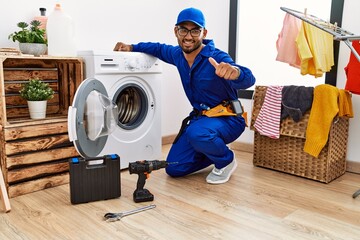 Wall Mural - Young indian technician working on washing machine approving doing positive gesture with hand, thumbs up smiling and happy for success. winner gesture.