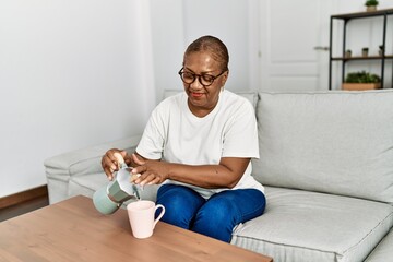 Wall Mural - Senior african american woman smiling confident pouring coffee on cup at home