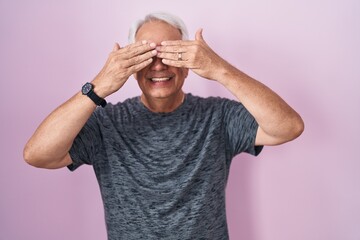 Sticker - Middle age man with grey hair standing over pink background covering eyes with hands smiling cheerful and funny. blind concept.