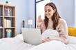 © Krakenimages.com - Young hispanic woman using computer laptop on the bed doing ok sign with fingers, smiling friendly gesturing excellent symbol