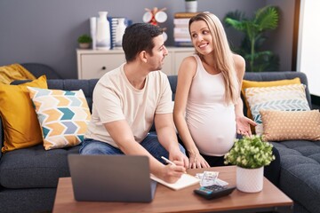 Canvas Print - Man and woman couple expecting baby writing on notebook accounting at home