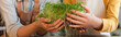 © LIGHTFIELD STUDIOS - Cropped view of friends in aprons holding microgreen at home, banner.