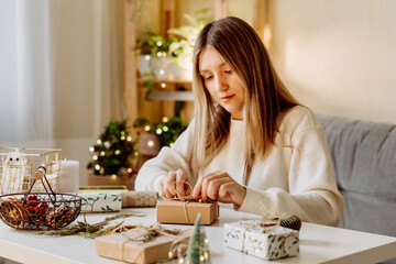 Wall Mural - Woman wrapping Christmas eco natural gift boxes at home. Preparing presents on white table with decor elements, lights and items Christmas or New year DIY packing Concept.