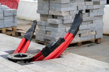 Metal base and red pvc pipes for urban street lighting come out of ground among laid granite paving stones on pedestrian sidewalk construction site