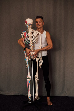 A man in a white T-shirt studies the structure of the human skeleton