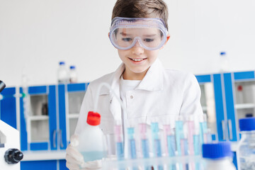 Canvas Print - smiling boy in goggles holding bottle near blurred test tubes during chemical experiment in laboratory.