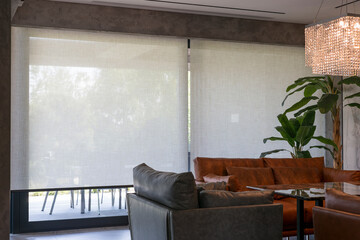 Wall Mural - Roller blinds in the interior. Automatic solar shades large size on the window. Living room interior with sofas and palm trees. Electric sunscreen curtains for home. 