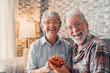 Portrait of two cute and old seniors at home having fun together. Mature man  giving a gift at his wife for Christmas or anniversary. Surprised pensioner woman looking at the camera..