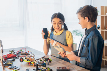 Canvas Print - amazed girl pointing at smartphone with blank screen near boy holding robotics hand at home.