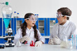 © LIGHTFIELD STUDIOS - amazed girl in goggles looking at friend near flask with red liquid in chemical lab.