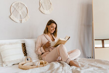 Pretty Smiling Woman Relaxing At Home On Bed In Morning In Pajamas Reading Book