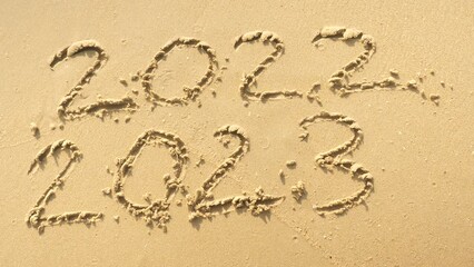 Wall Mural - message year 2022 replaced by 2023 written on beach sand background. goodbye 2022 hello to 2023 lapp