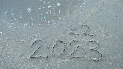 Wall Mural - message year 2022 replaced by 2023 written on beach sand background. goodbye 2022 hello to 2023 lapp