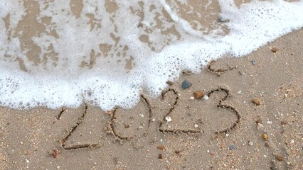 Wall Mural - message year 2022 replaced by 2023 written on beach sand background. goodbye 2022 hello to 2023 lapp