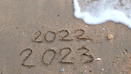 Wall Mural - message year 2022 replaced by 2023 written on beach sand background. goodbye 2022 hello to 2023 lapp