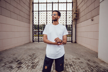 Wall Mural - African american man in a white blank t-shirt walks down the street. Mock-up.