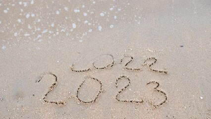 Wall Mural - Message Year 2022 replaced by 2023 written on beach sand background. 
Goodbye 2022 hello to 2023 Lapping waves happy New Year coming concept.