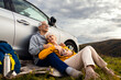 © Zoran Zeremski - Senior couple sitting against the car, resting after hiking in countryside.