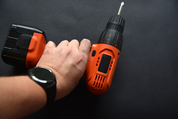 Wall Mural - Orange screwdriver on a black background in the hand. Screwdriver and electric drill with power supply