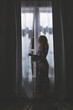 © DTowersPhoto - Silhouette of woman looking out window through curtains at nighttime in the dark