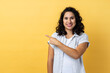 Portrait of smiling satisfied beautiful woman with dark wavy hair standing pointing aside with finger, showing copy space for advertisement. Indoor studio shot isolated on yellow background.