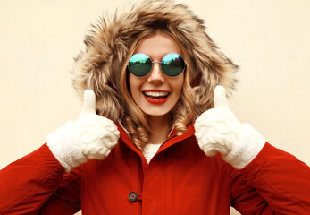 Wall Mural - Portrait of happy surprised laughing young woman showing finger gesture thump up wearing red jacket with fur hood and mittens