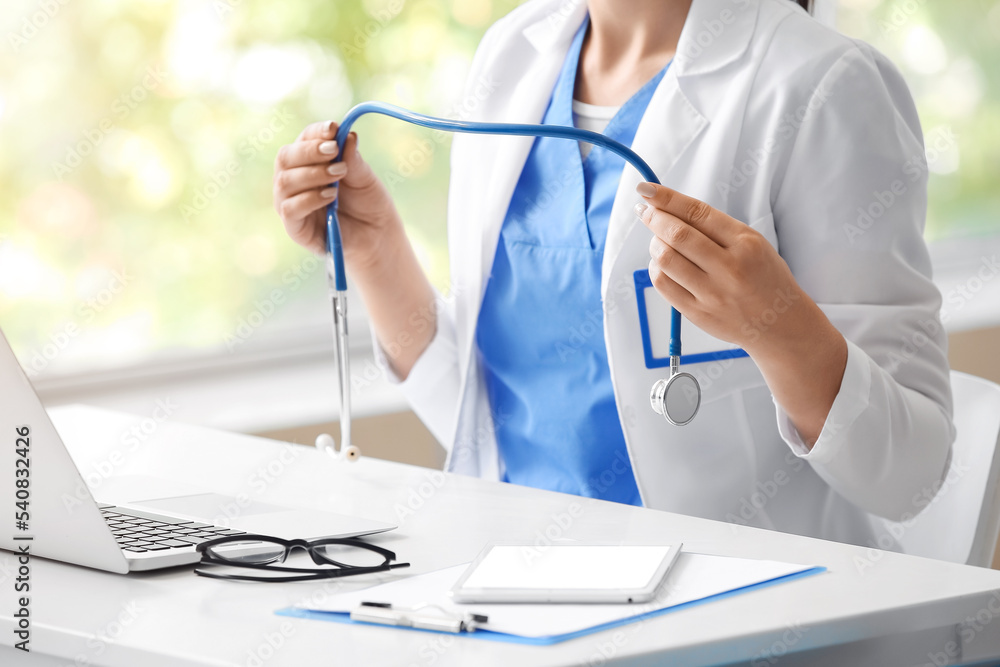 Female doctor with stethoscope sitting at table with laptop and tablet computer