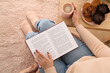 © Pixel-Shot - Woman with cup of coffee reading book at home