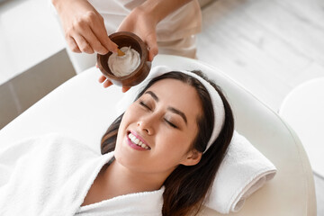 Wall Mural - Beautician applying mask on face of young Asian woman in spa salon