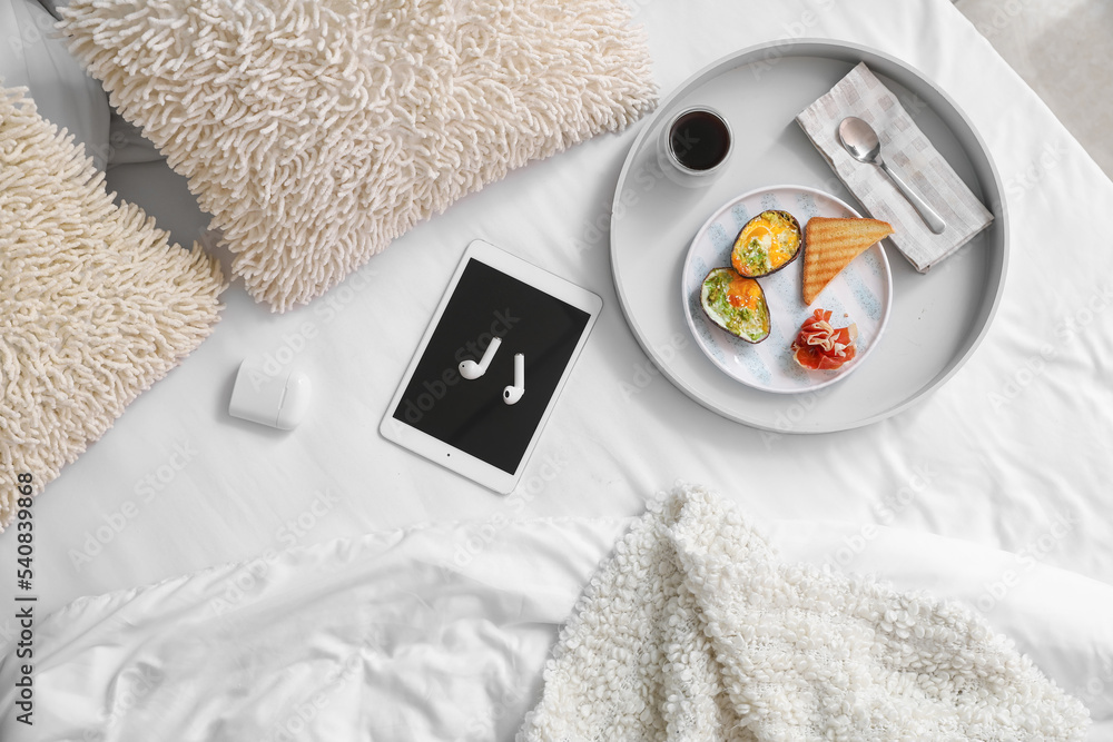 Tray with delicious breakfast, tablet computer and earphones on bed