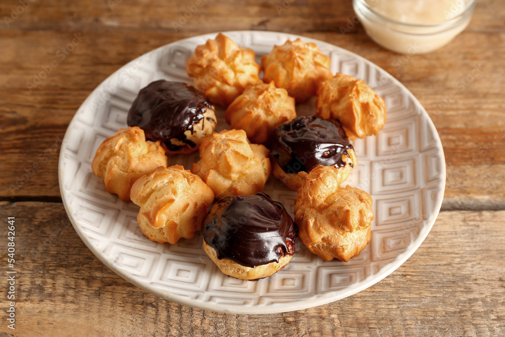 Plate with delicious eclairs on wooden background, closeup