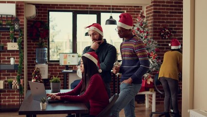 Wall Mural - Diverse coworkers working on startup report in festive office, doing teamwork at desk during christmas time. Brainstorming ideas on computer in space decorated with holiday ornaments.