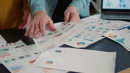 Wall Mural - Selective focus on colleagues comparing marketing statistics and working on business strategy at desk with laptop. Detail view of coworkers hands going through papers with sales charts.