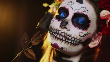 Wall Mural - Scary lady of death with skull and colorful wreath of flowers posing in studio, using black rose to be glamorous and creepy. Woman with festival make up and mexican ritual costume. Handheld shot.