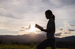 © Tinnakorn - Silhouette of woman praying to god with bible on mountain at sunset background. Woman raising his hands in worship. Christian Religion concept.