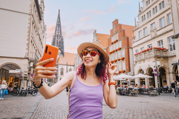 Wall Mural - Happy tourist girl taking selfie photo while visiting Prinzipalmarkt street and admiring old town architecture buildings in Munster, Germany