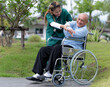 A physiotherapist Asian woman in green clothes helps an elderly man exercise on a wheelchair in a nursing home, nursing care.