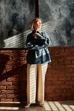 Portrait Of Mature Woman In Stylish Clothes Standing Against Brick Wall At Studio