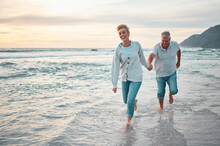 Beach, Walking And Senior Couple Holding Hands For Support, Love And Care With Outdoor Wellness, Retirement And Holiday Lifestyle With Sunset Sky. Elderly People Running Together In Sea Ocean Water