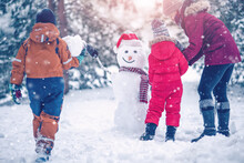 Family Bilding A Cute Snowman In The Snowy Park.