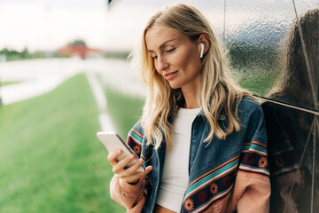 blonde woman outdoors using mobile phone for social media chat.